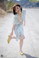 A woman in a blue dress and yellow shoes on a road.