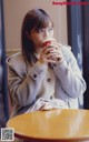 A woman sitting at a table drinking from a cup.
