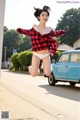 A woman jumping in the air in front of a blue car.