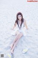 A woman in a white dress sitting on a sandy beach.