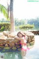 A woman in a pink bikini laying on a rock in a pool.